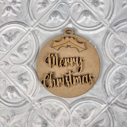 A "Round Christmas Ornament" from Janet's Craft Corner's DIY Decoration Kits complements your home décor when placed elegantly on a decorative white textured surface. Featuring a charming holly design at the top, this ornament adds a festive touch to any setting with its "Merry Christmas" text.