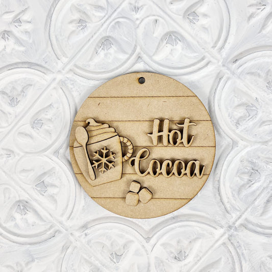 The Hot Cocoa Round Ornament by Janet's Craft Corner is a charming DIY décor piece. With its wooden mug design adorned with a candy cane, snowflake pattern, "Hot Cocoa" text, and three marshmallow shapes on a textured white background, it adds whimsical flair to your holiday setup.