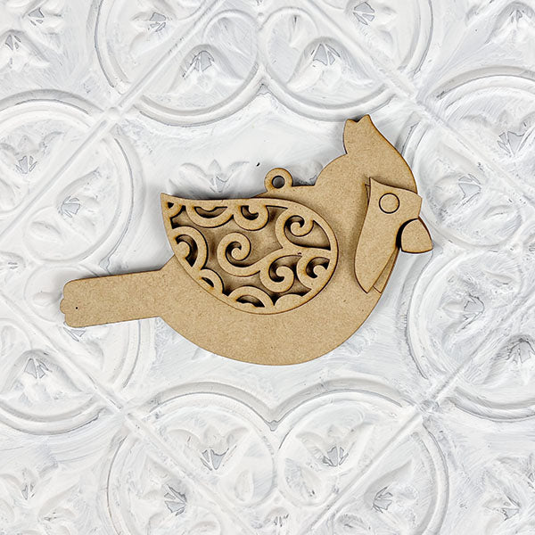 Introducing the Cardinal Ornament from Janet's Craft Corner—a DIY decoration kit featuring a cardinal bird crafted from wood, adorned with intricate swirl patterns on its wings and set against a white embossed, patterned background. Ideal for holiday décor or as a hand-painted craft project.