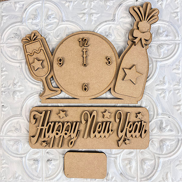 The New Year Interchangeable Insert from Janet's Craft Corner is a hand-painted wooden craft decoration featuring a clock striking midnight alongside a champagne bottle and glass. The words "Happy New Year" are elegantly carved in script against a textured white background, making it an ideal addition to your interchangeable home decor collection.