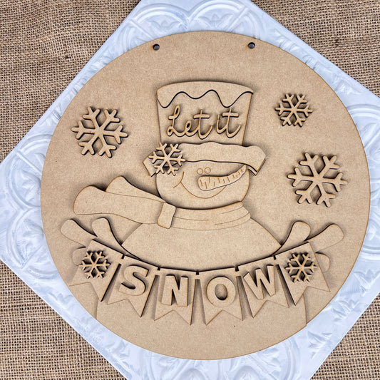 Create charming holiday decor with Janet's Craft Corner's DIY kit: the Snowman Let It Snow Door Hanger, featuring a smiling snowman in a top hat that reads "Let it" and banner saying "SNOW" on burlap, perfect for any seasonal project.