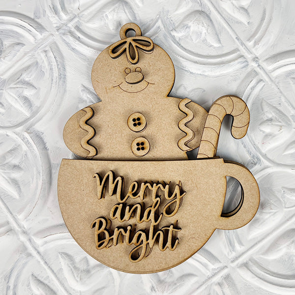 This delightful ornament from Janet's Craft Corner, ideal for holiday decor, features a gingerbread person with buttons smiling above a teacup. The cup boasts a candy cane handle and the engraving "Merry and Bright," perfectly completing the Gingerbread Teacup Ornaments against a textured white backdrop.