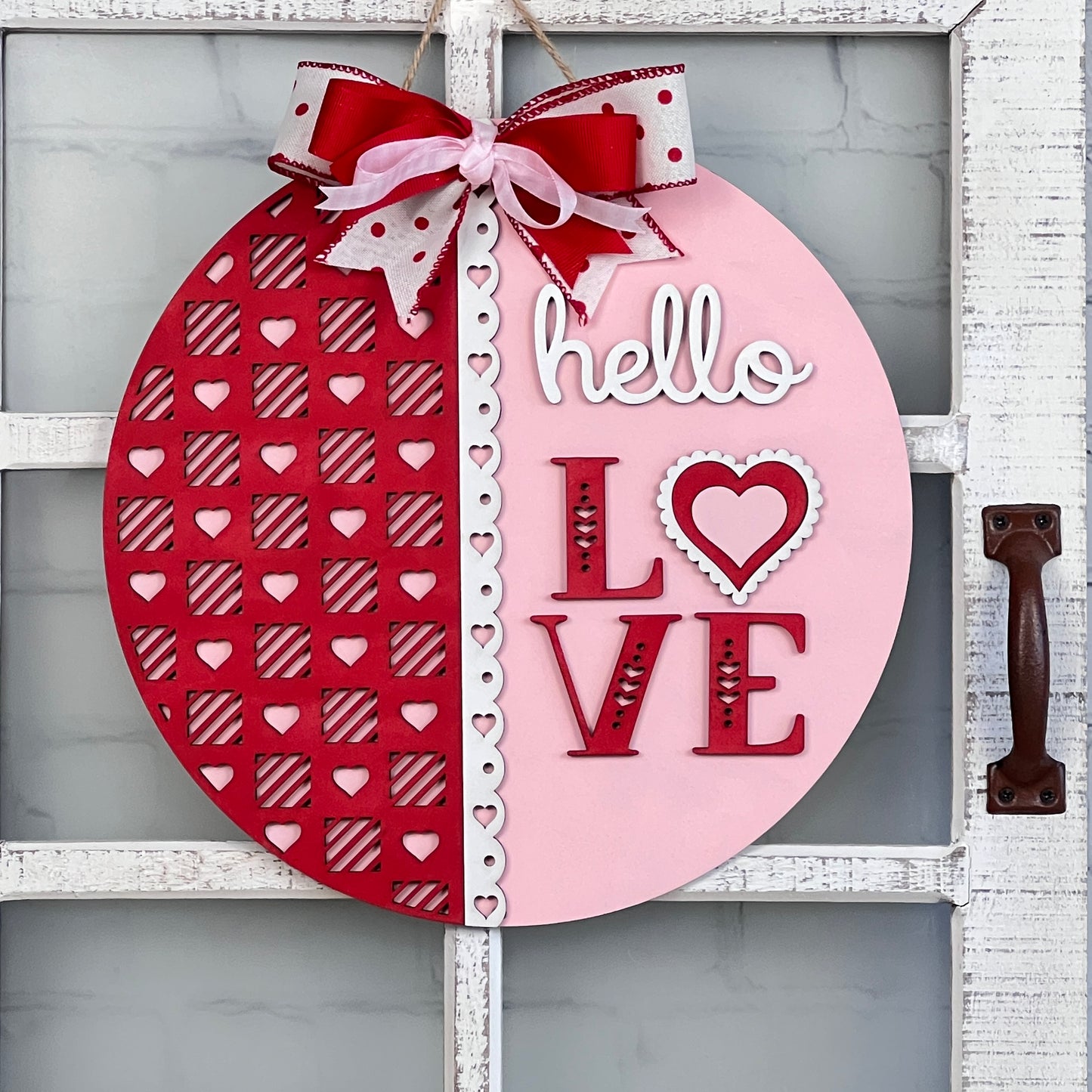 Introducing Janet's Craft Corner's "Hello Love Round Sign" DIY Kit: Delight in creating a beautiful piece of home decor that's perfect for Valentine's Day. This round sign features a sophisticated "hello LOVE" script, with the left half displaying a vibrant red hue adorned with heart patterns and the right half in a soft pink shade. It is elegantly finished with a charming red and white bow.