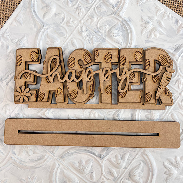 Janet's Craft Corner offers the Easter Trio Mini Shelf Sitters, wooden decorations that feature the word "Easter" with "happy" inscribed across it. Ideal as Easter decor, these sitters have letters adorned with carved egg designs and a carrot and flower embellishment at each end. They come with a separate rectangular base, making them perfect for cheerful display on a shelf.