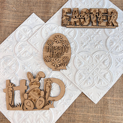 Janet's Craft Corner presents the Easter Trio Mini Shelf Sitters DIY kit, a set of 3 wooden pieces: "Happy Easter" sign, an egg shape with "Hippity Hop," and a "Hop" sign with bunny and carrots, all hand-painted with floral designs to elevate your Easter decor.