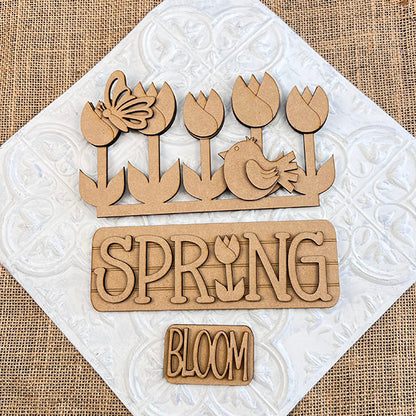 The Spring Tulips Interchangeable Insert from Janet's Craft Corner is a delightful DIY home decor kit that includes hand-painted wooden cutouts with a floral and spring theme. Featuring tulips, a butterfly, a bird, and the words "SPRING" with a tulip in place of the letter "I" and "BLOOM," this craft kit allows you to easily update your seasonal display.