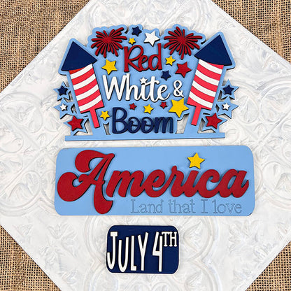 The Red White & Boom Interchangeable Insert - Painted by Janet's Craft Corner features colorful fireworks and stars, celebrating American Pride with the text "Red, White & Boom" at the top, "America, Land that I love" in the middle, and "July 4th" at the bottom. This decorative piece is perfect for enhancing your home decor with its textured background flair.