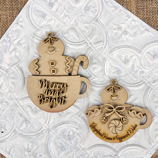 Two delightful wooden gingerbread ornaments lie on a textured white surface. One ornament, from Janet's Craft Corner, displays a Gingerbread Teacup design featuring the phrase "Merry and Bright," while the other highlights a peppermint motif adorned with the words "Gingerbread Houses & Peppermint Wishes." These pieces make perfect additions to your holiday decor.