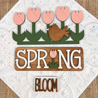 Introducing the "Spring Tulips Interchangeable Insert" from Janet's Craft Corner – a DIY home decor kit that showcases a delightful spring-themed design. This artwork features pink tulips and a brown bird set against a white background, with the word "SPRING" prominently displayed and cleverly incorporating a tulip for the letter "I." A smaller accompanying sign reads "BLOOM.