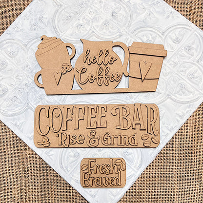 The Coffee Bar Interchangeable Insert from Janet's Craft Corner is a DIY home decor kit featuring hand-painted coffee-themed cutouts. It includes a teapot and cups with "hello Coffee," a "COFFEE BAR" sign with "Rise & Grind," and a small "Fresh Brewed" sign, all set against textured white tiles. Beautifully arranged on burlap fabric, these inserts are perfect for adding charm to your space.