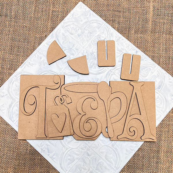 From Janet’s Craft Corner, the "Tea Word Block Shelf Sitter" DIY kit includes a spoon, heart-adorned teabag, and decorative elements on burlap with cutout letters forming "TEA," anchored by a textured white square—a delightful home décor addition.