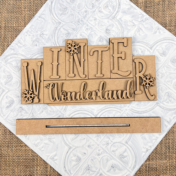 Enhance your home with Janet's Craft Corner's Winter Wonderland Mini Word Block Shelf Sitter. This DIY seasonal decor kit, adorned with elegant snowflakes on a textured white and burlap backdrop, is perfect for craft enthusiasts seeking festive charm.