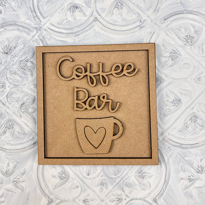 The Coffee Swappable Squares DIY craft kit from Janet's Craft Corner features a wooden sign with "Coffee Bar" above a coffee cup with a heart—perfect for your next coffee-inspired project or seasonal home decor makeover.