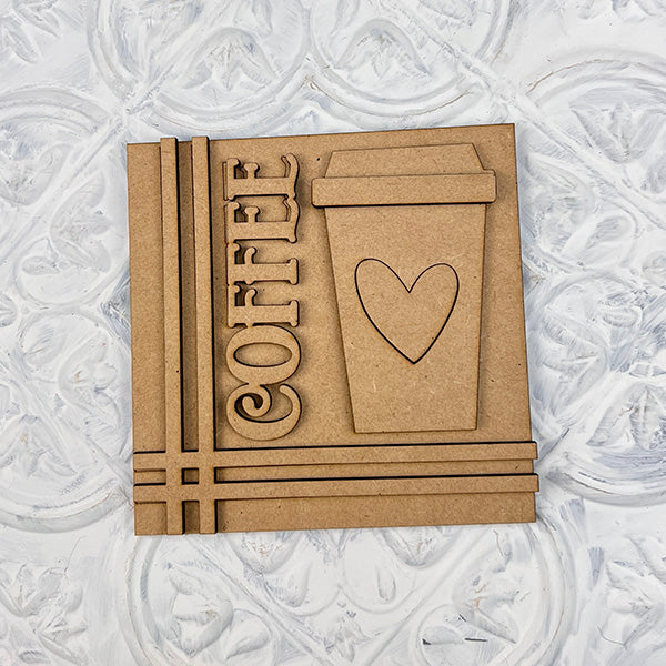 Janet's Craft Corner Coffee Swappable Squares DIY kit: A square coaster with "COFFEE" cut out vertically, an engraved cup with heart, and a textured white background—ideal for coffee lovers or creative home decor projects.