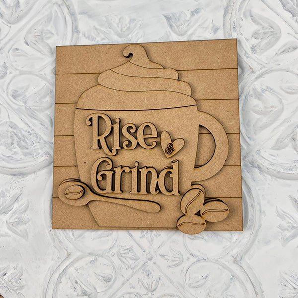 The Coffee Swappable Squares DIY craft kit by Janet's Craft Corner features a wooden coffee cup cutout with whipped cream, beans, spoon, and “Rise & Grind” text—perfect for coffee lovers or unique seasonal home decor.