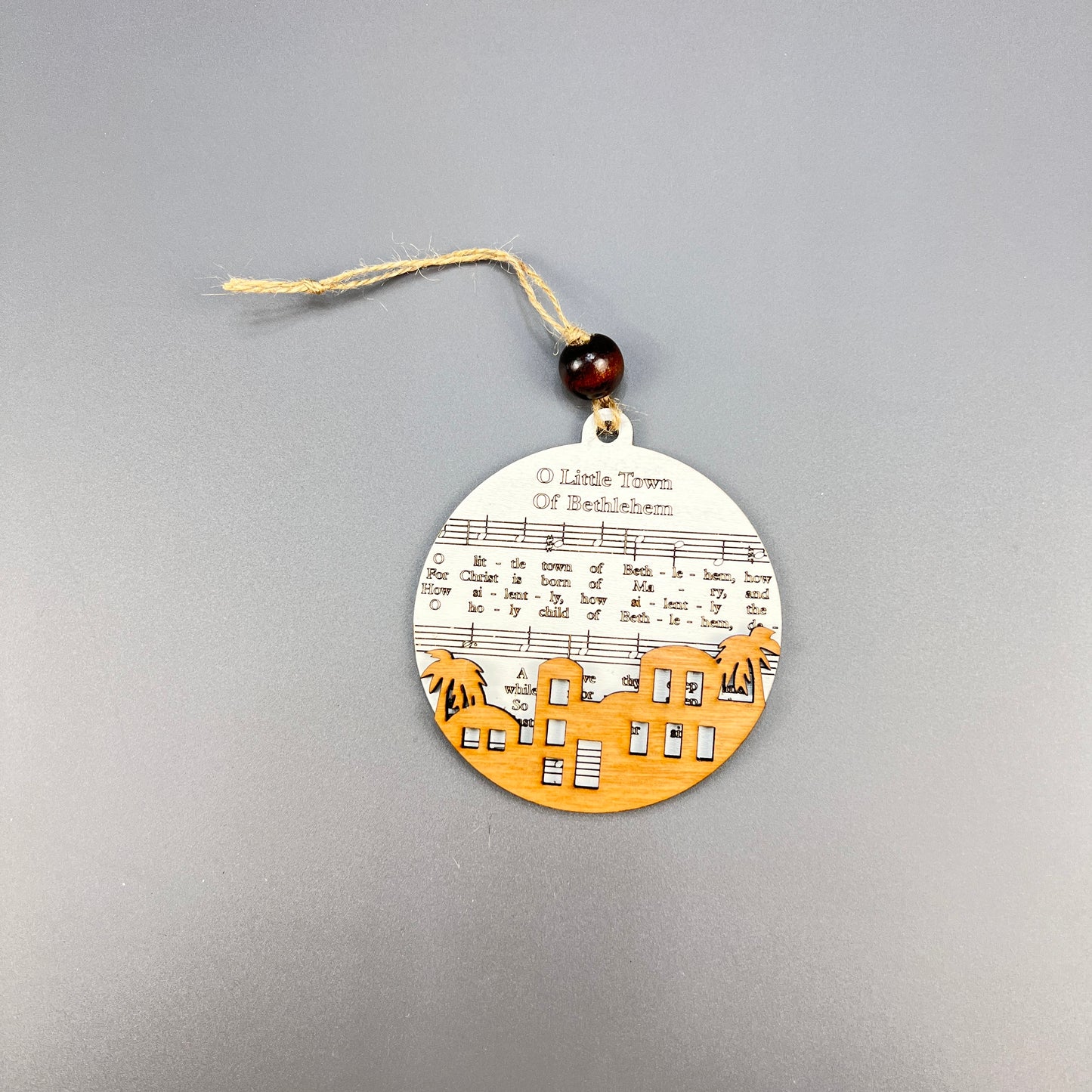 Janet's Craft Corner presents the Sheet Music Ornaments, a rustic charm that features the sheet music of "O Little Town of Bethlehem" accompanied by a wooden cutout skyline. Perfect for music lovers, this ornament includes a string for hanging and is adorned with a dark bead, making it an ideal addition to your holiday decor.