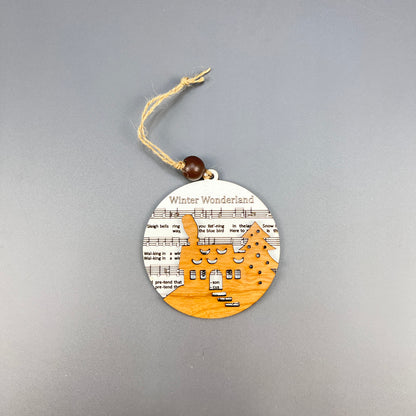 Discover the rustic charm of Janet's Craft Corner's Sheet Music Ornament, ideal for music enthusiasts. This ornament showcases a laser-cut wooden reindeer amidst snow-covered trees, all set against the backdrop of sheet music titled "Winter Wonderland." A twine loop with a wooden bead finishes off this charming piece.