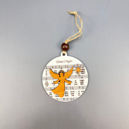 Introducing the Sheet Music Ornament from Janet's Craft Corner: This round ornament showcases a musical staff with notes and bears the title "Silent Night." Adorned with an orange angel silhouette for rustic charm, it is completed with a hanging string threaded through a wooden bead—an ideal gift for music lovers.