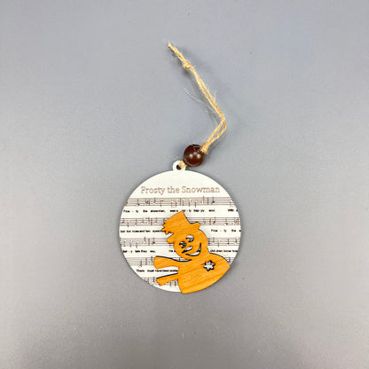 The Sheet Music Ornaments from Janet's Craft Corner are ideal for music enthusiasts, showcasing a round wooden snowman embellished with an orange top hat and scarf. The ornament is set against a rustic backdrop of "Frosty the Snowman" sheet music and includes a string with a bead for easy hanging.