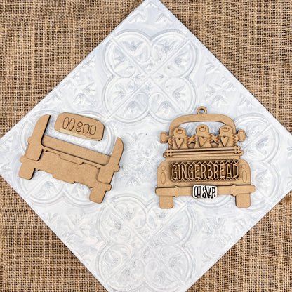 A pair of wooden cutouts depicting vintage trucks is set against a white textured backdrop. One of the trucks is plain, while the other, an Antique Truck Ornament from Janet's Craft Corner's DIY Decoration Kits, showcases "Gingerbread Oh Snap" along with gingerbread figures and heart details on its bed. The scene rests atop patterned white tiles over burlap, making it ideal for Christmas décor.