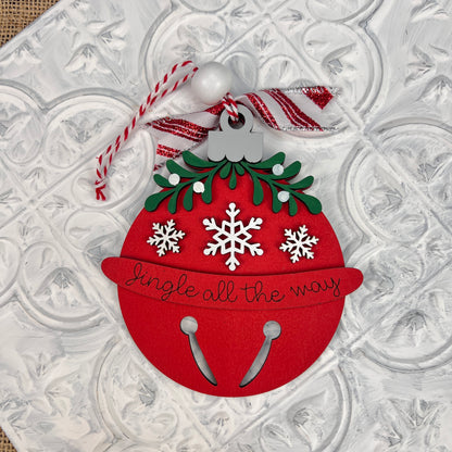 Janet's Craft Corner offers a Mistletoe Ornaments DIY Decor Kit, featuring ornaments in red jingle bell shapes with green leaves, white snowflakes, and "jingle all the way" text. Adorned with silver, red, and white ribbons, they're perfect for personalized home décor against a textured white background.