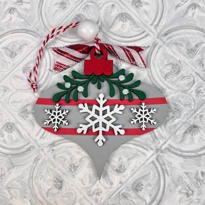 Craft festive charm with Janet's Craft Corner Mistletoe Ornaments DIY Decor Kit. The set of six includes teardrop-shaped ornaments adorned with white snowflakes, green mistletoe leaves, a red bow, and a red and white hanging cord, all standing out against a textured white background.