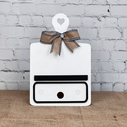 Janet's Craft Corner offers the Breadboard Interchangeable Base with Insert DIY kit. This decorative white board has a heart handle, gingham bow, minimalistic face markings, and interchangeable accessories—ideal for DIY enthusiasts against a burlap backdrop.