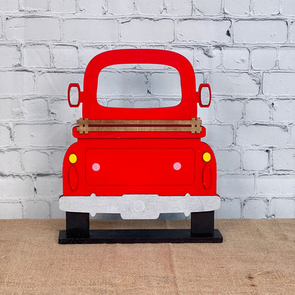 The Antique Truck Interchangeable Base - Painted by Janet's Craft Corner is a red wooden cutout, shown from the rear on burlap against a white brick wall. This charming decor piece makes perfect interchangeable seasonal decor.