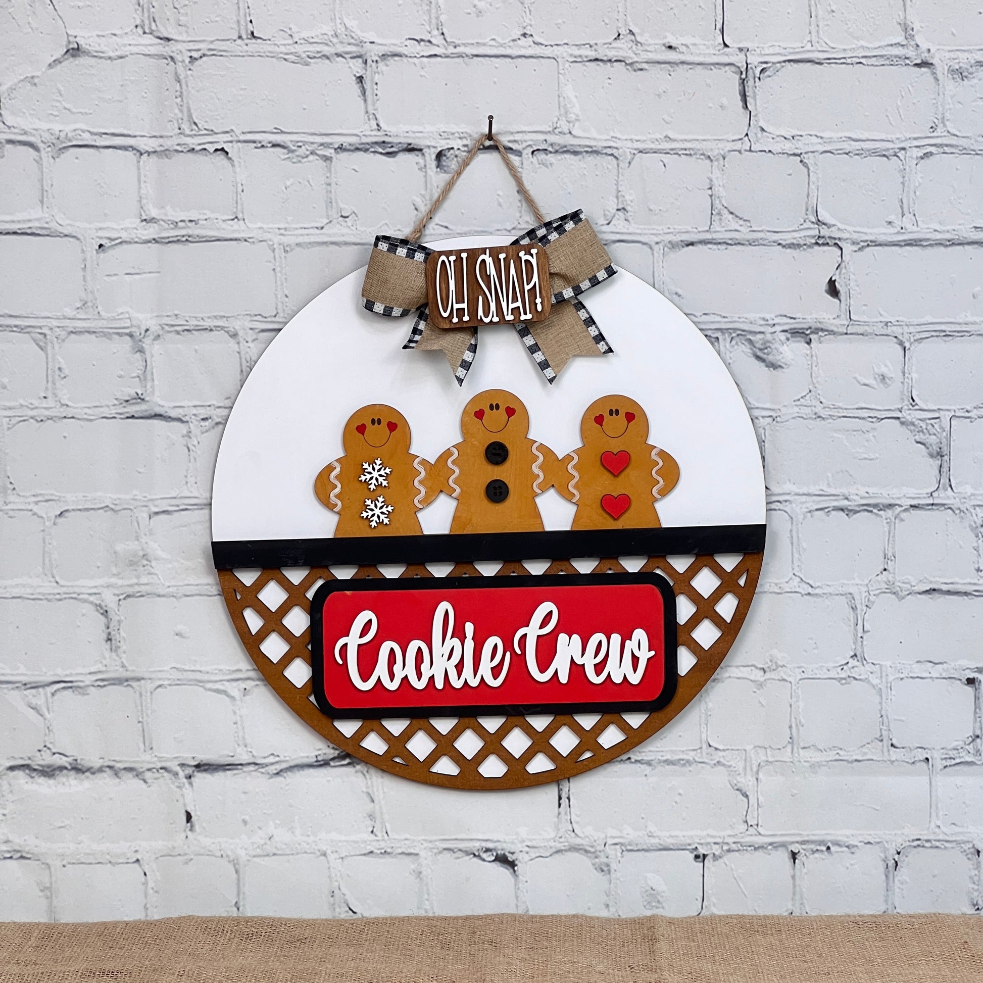 The Cookie Crew Interchangeable Insert by Janet's Craft Corner is a DIY seasonal decor kit with 3 pieces, featuring gingerbread men designs and festive "OH SNAP" and "Cookie Crew" text on a white brick wall background.