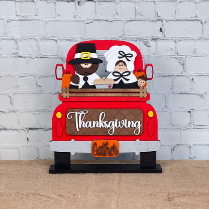 Janet's Craft Corner offers a Pilgrim Interchangeable Insert as part of their DIY home decor kit, featuring a red truck with a pilgrim couple, pie, and corn. "Thanksgiving" and "Gather" appear on the tailgate, set against a white brick wall—perfect for charming Thanksgiving decor.