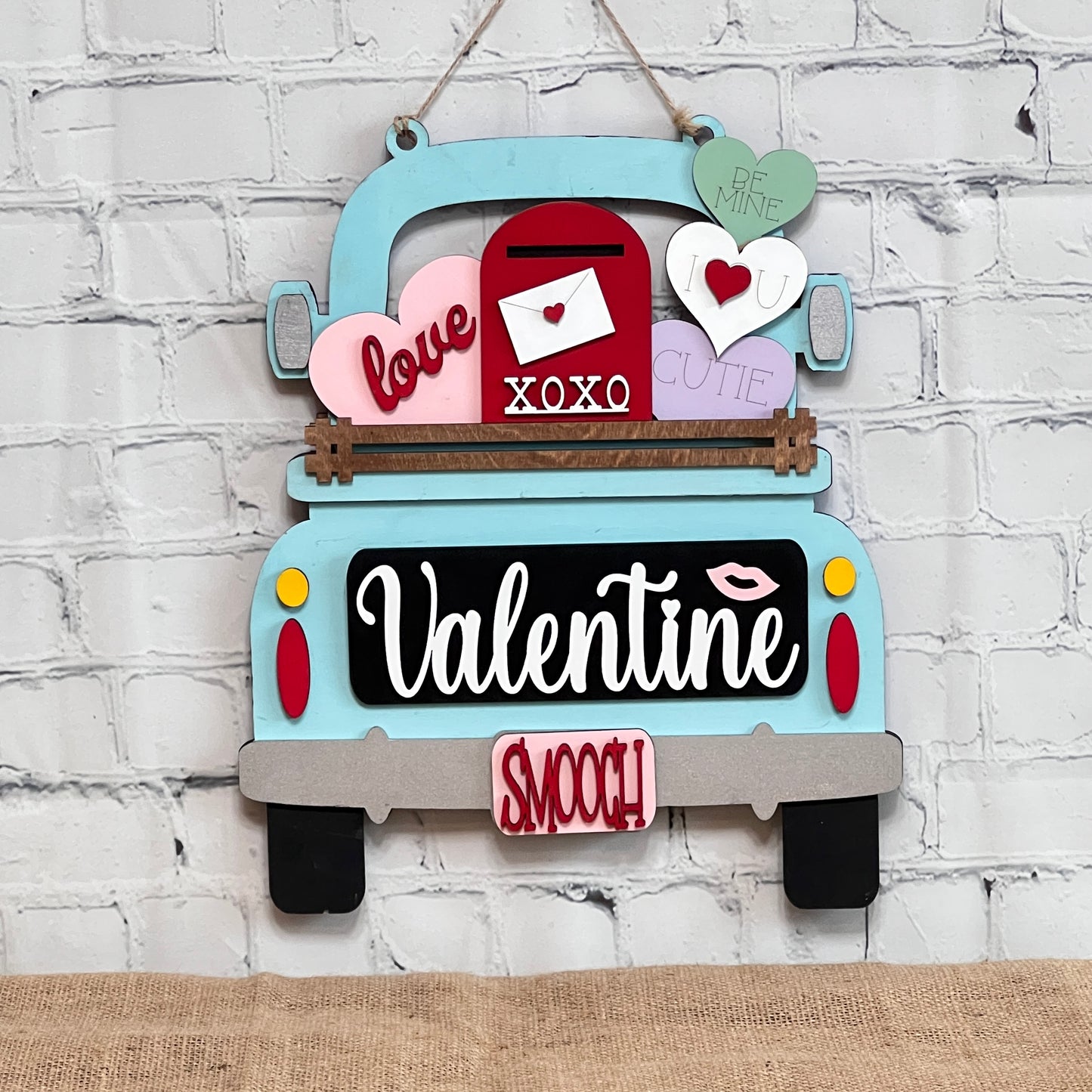 Janet's Craft Corner offers the Valentine Interchangeable Insert DIY home decor kit, a decorative wooden sign shaped like a vintage truck with hearts and an envelope, featuring words like "love," "XOXO," and "cutie." Ideal for Valentine's Day, it hangs beautifully on a white brick wall.