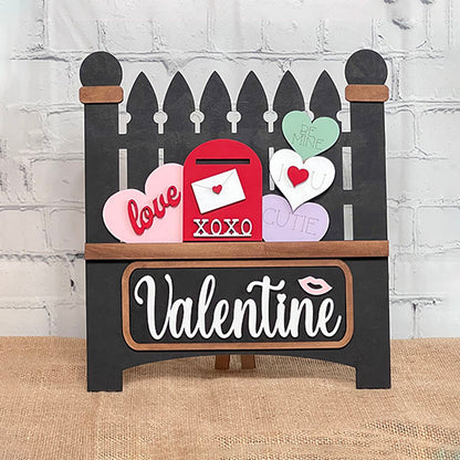 The Valentine Interchangeable Insert by Janet's Craft Corner is a DIY home decor kit featuring a black picket fence with heart-shaped messages, a red "XOXO" mailbox, "Valentine" text, and an interchangeable insert for customization.