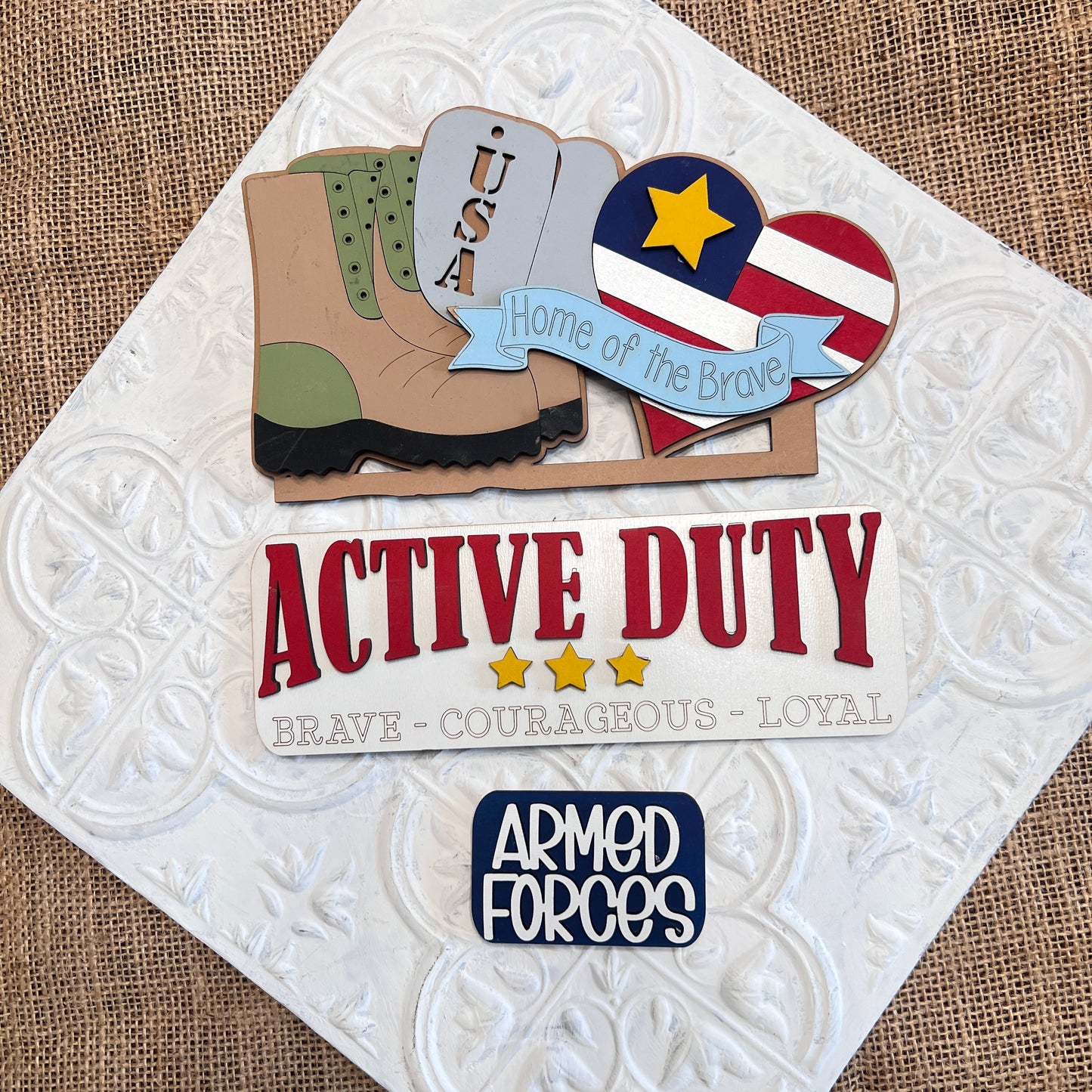 Enhance your craft collection with Janet's Craft Corner's Military Interchangeable Insert DIY home decor kit. The set includes military-themed embellishments: a "USA" boot, a stars and stripes heart, and the phrases "Home of the Brave," "Active Duty," and "Brave, Courageous, Loyal.