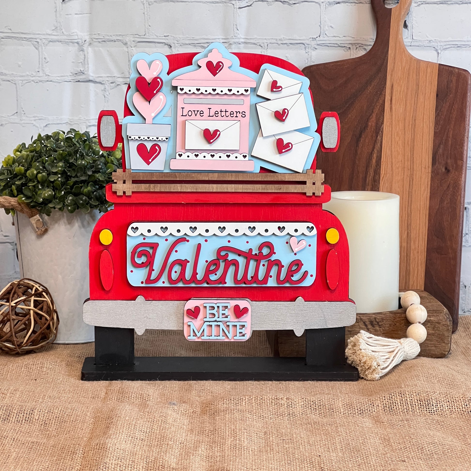 Janet's Craft Corner presents an Antique Truck Base with Insert DIY kit, featuring a wooden truck adorned with "Love Letters," hearts, a "Valentine" sign, and a "Be Mine" bumper. Ideal for craft lovers, this display is perfect alongside cutting boards or near candles and plants.