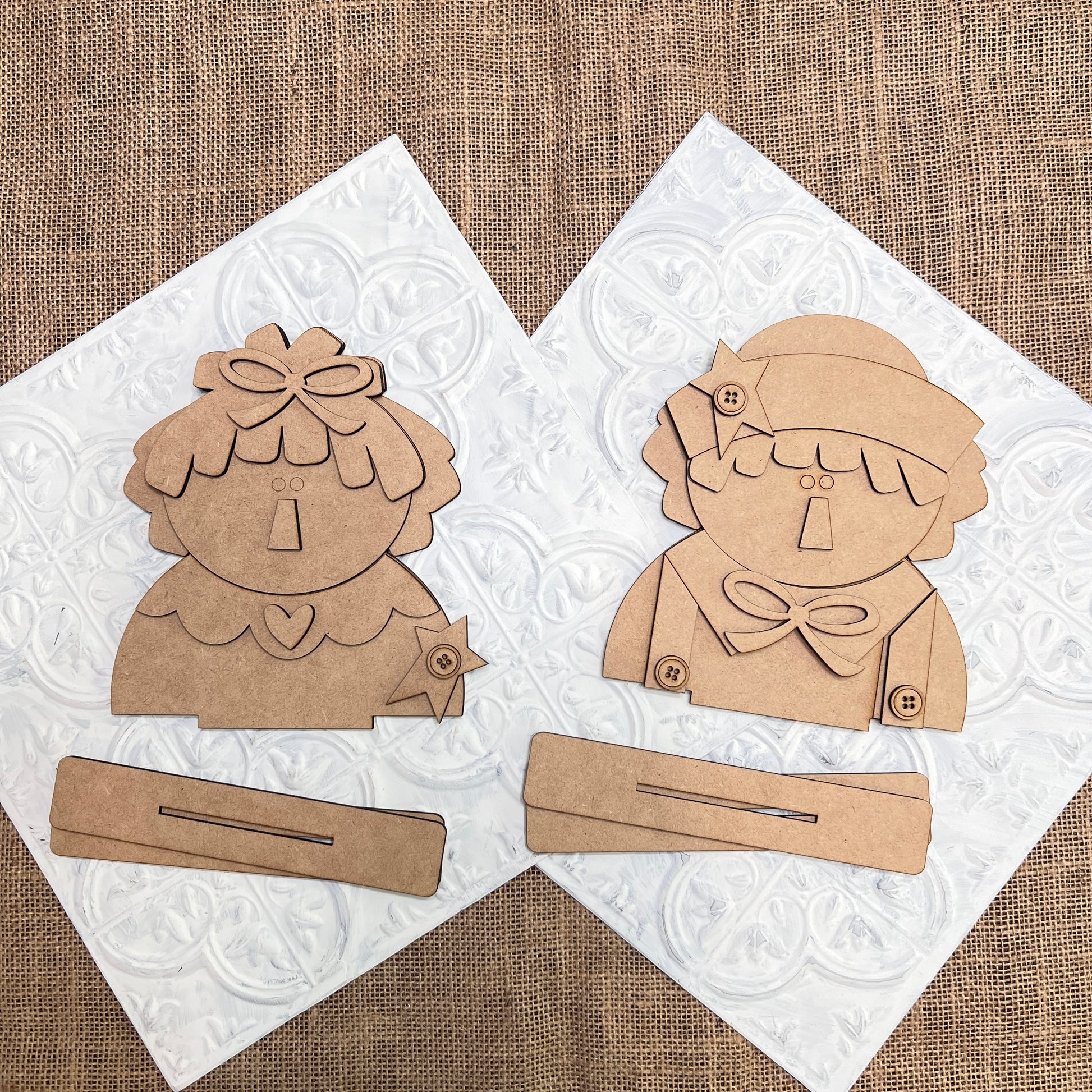 Janet's Craft Corner Raggedy Ann & Andy Shelf Sitters DIY kit includes two unfinished wooden cutouts with bases—one doll has a bow and collar, the other a hat and scarf—perfect for creating charming seasonal home decor. Set of 1.