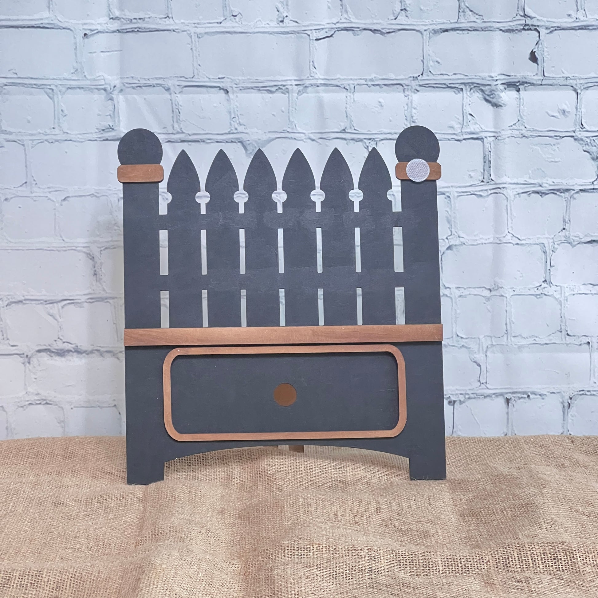 The Garden Fence Interchangeable Base - Painted by Janet's Craft Corner is a small decorative wooden shelf with a picket fence design, gray paint, brown trim, and a bottom drawer—perfect for DIY decor.