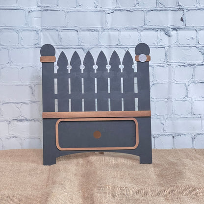 The Garden Fence Interchangeable Base - Painted by Janet's Craft Corner is a small decorative wooden shelf with a picket fence design, gray paint, brown trim, and a bottom drawer—perfect for DIY decor.