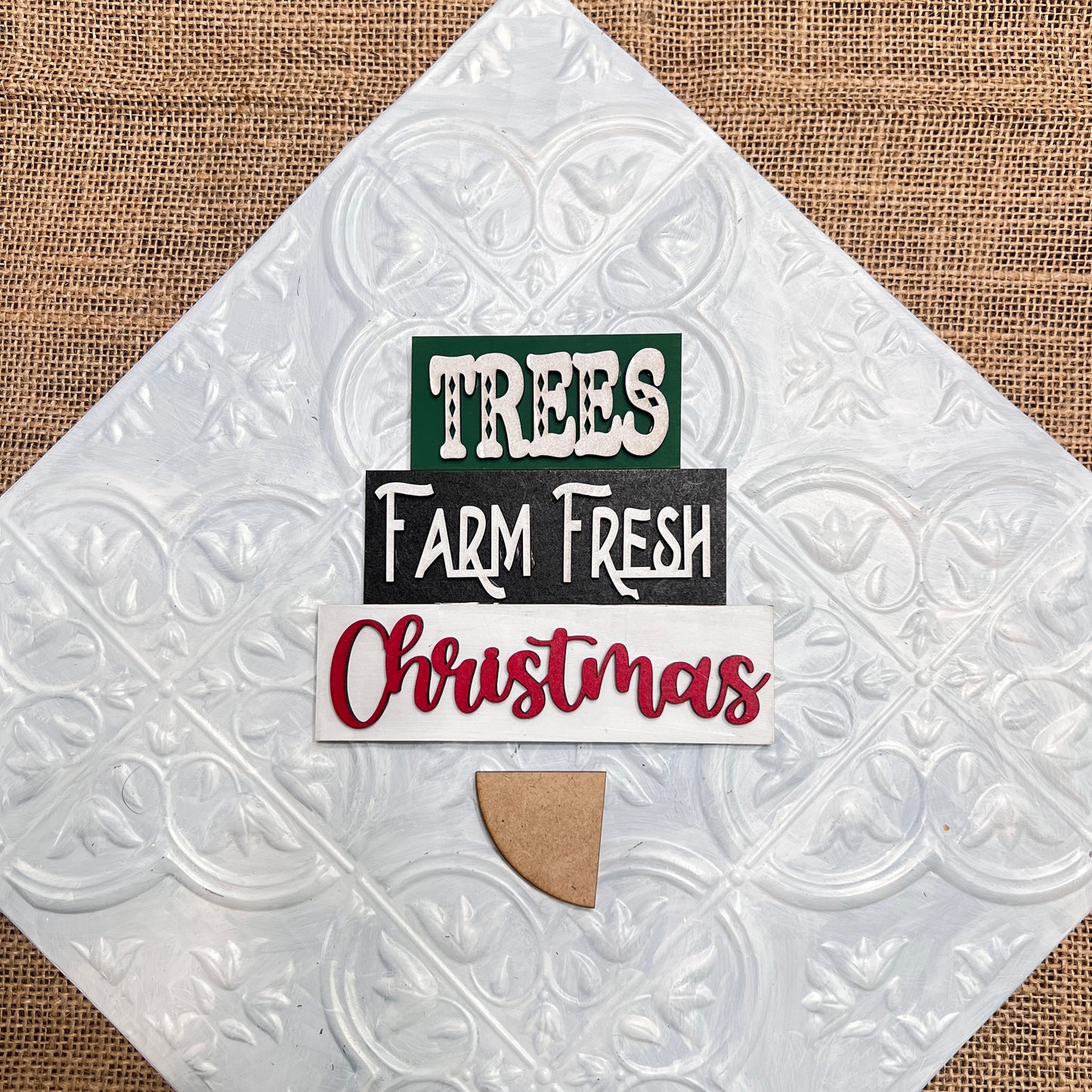 The Word Stacks - Painted sign from Janet's Craft Corner features "TREES" in green, "Farm Fresh" in white on black, and "Christmas" in red on a textured white background with a tan wood accent at the bottom.