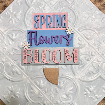 Janet's Craft Corner Word Stacks - Painted features a three-layer decorative sign that reads "SPRING Flowers BLOOM," with colorful letters, two white daisies, and floral patterns on a textured white background.