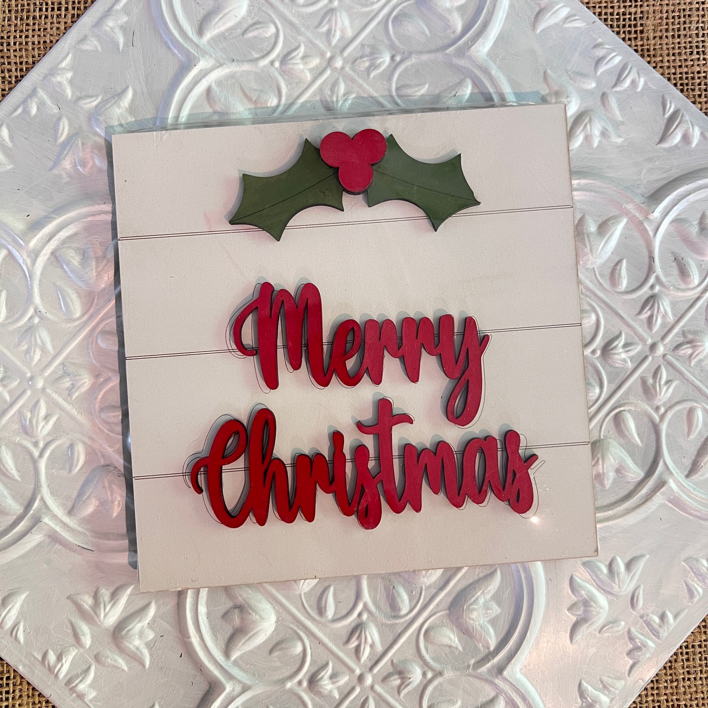 A festive 6 inch square from Janet's Craft Corner features red "Merry Christmas" text with green holly and red berries on a white embossed tile background.