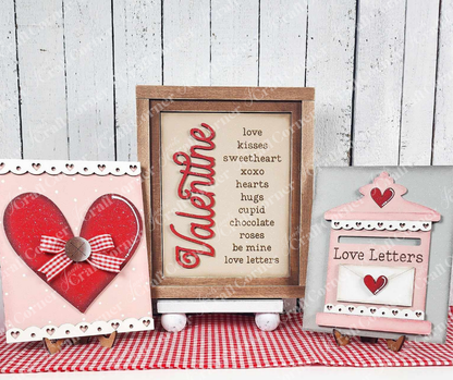 Three decorative Valentine's Day pieces on a gingham cloth: left, heart design with lace; center, "Valentine" text with romantic words; right, pink mailbox with "Love Letters." From Janet's Craft Corner, this Farmhouse Frame for Interchangeable Signs kit adds charm to any space.