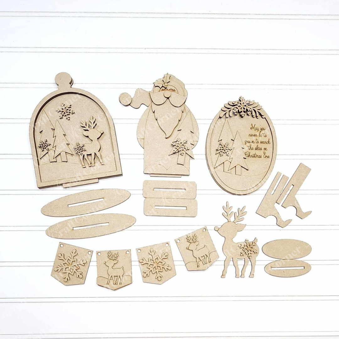 A flat lay of the unassembled "Oh Deer Decor Set" by Janet's Craft Corner is displayed on a white surface, showcasing wooden Christmas decorations that include a Santa, reindeer, trees, ornaments, and holiday message plaques. This DIY craft kit features festive cut-out designs perfect for interlocking or hanging as charming home décor pieces.