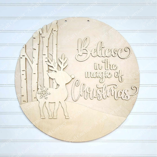 The "Oh Deer Door Hanger" by Janet's Craft Corner is a delightful round wooden sign ideal for home décor, showcasing a cut-out design of a reindeer and birch trees on the left side. On the right, it displays the phrase "Believe in the magic of Christmas" in elegant script lettering.