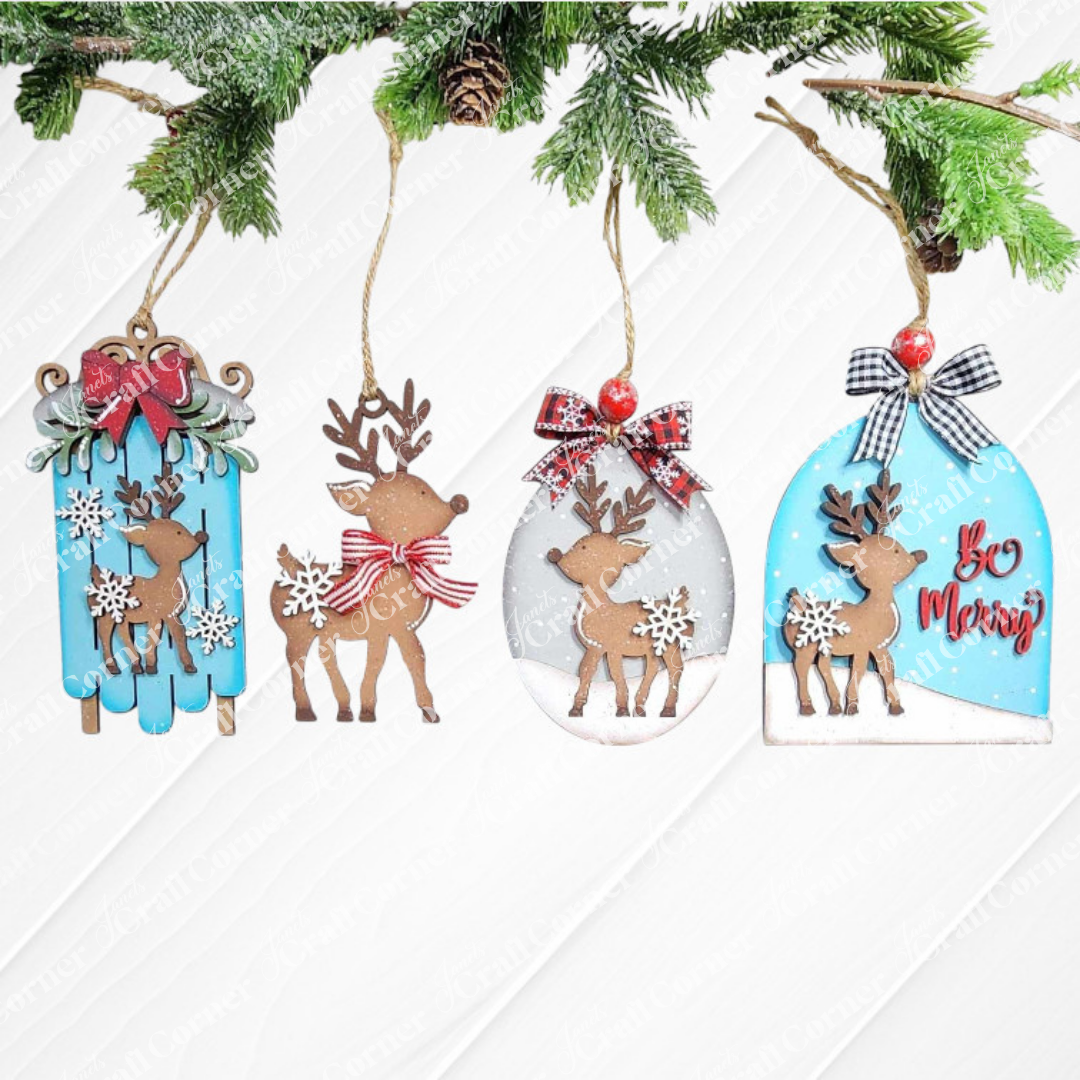 The Oh Deer Ornament Set from Janet's Craft Corner includes four Christmas ornaments that adorn a pine branch. Each piece showcases a reindeer silhouette surrounded by snowflakes and bows, set against unique backgrounds: sled, oval, circle, and bell shapes with the phrase "Be Merry." This DIY Craft Kit provides hand-painted home décor in a palette of brown, red, blue, and white tones.