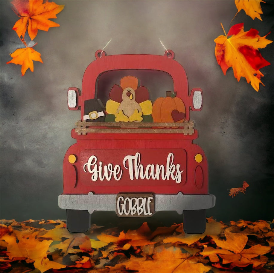 Introducing the "Give Thanks Interchangeable Insert" DIY home decor kit by Janet's Craft Corner. This charming wooden red truck features the phrases "Give Thanks" and "Gobble," with a truck bed carrying a turkey, pumpkin, and pilgrim hat. Surrounded by autumn leaves on a grey background, this piece is perfect as an interchangeable insert or for crafting enthusiasts to enjoy as a delightful DIY project.