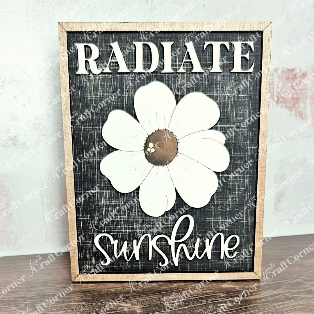 Janet's Craft Corner presents the Radiate Sunshine Farmhouse Sign, featuring a hand-painted large white flower and uplifting text on a dark background. This rustic decor DIY craft kit is perfect for infusing any space with positivity and cozy charm.