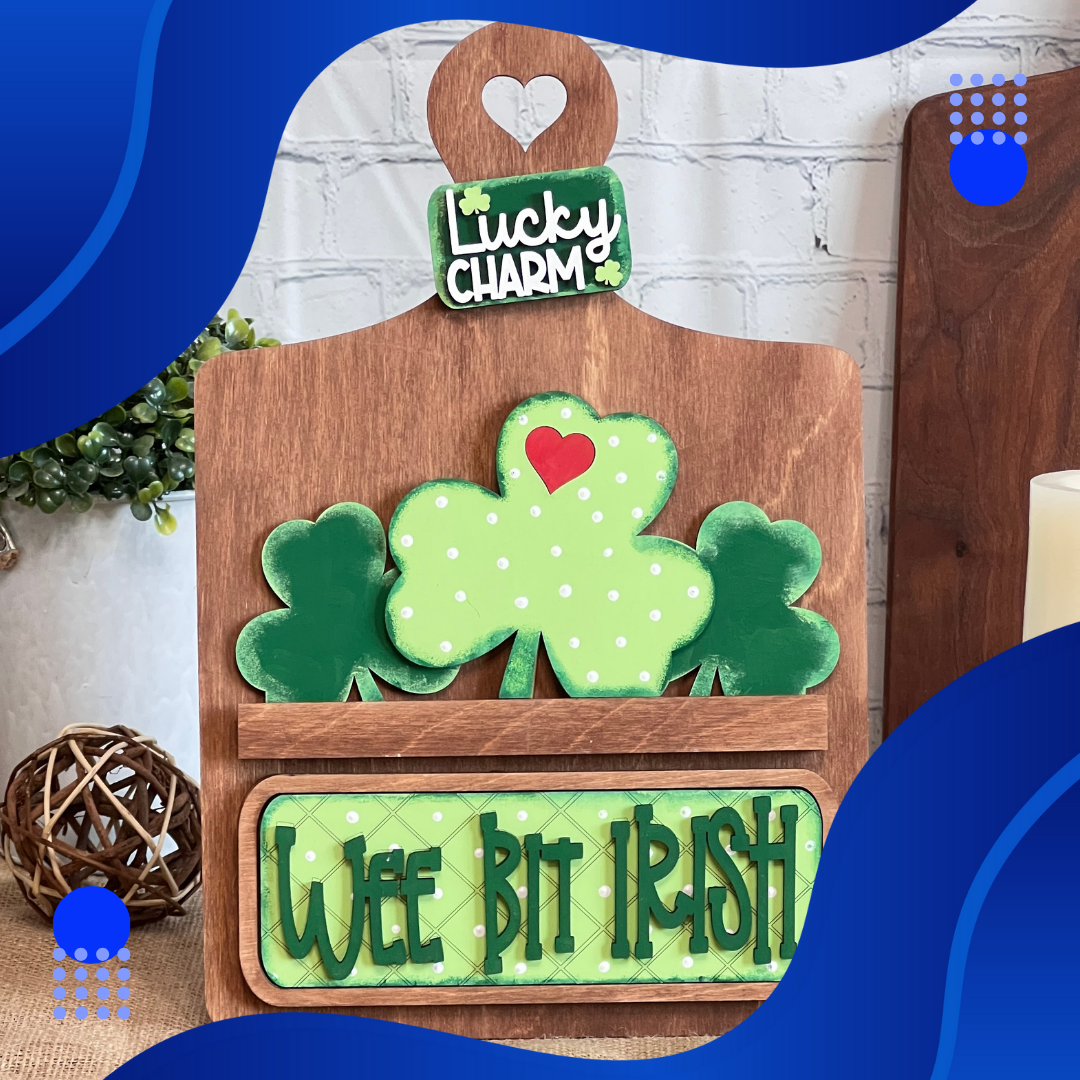 Janet's Craft Corner presents the "Wee Bit Irish Interchangeable Insert." This rustic wooden decor features green shamrocks and the phrases "Lucky Charm" and "Wee Bit Irish," accented with a red heart. It's set against a white brick background with blue abstract borders for added charm.
.