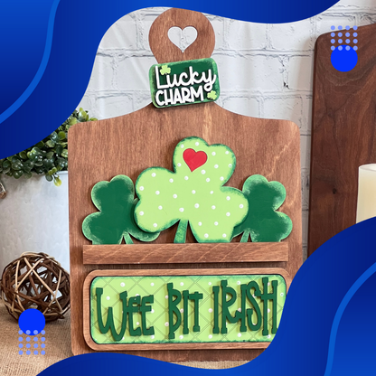 Janet's Craft Corner presents the "Wee Bit Irish Interchangeable Insert." This rustic wooden decor features green shamrocks and the phrases "Lucky Charm" and "Wee Bit Irish," accented with a red heart. It's set against a white brick background with blue abstract borders for added charm.
.