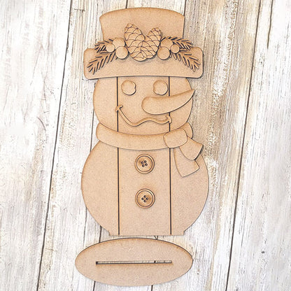 Introducing Janet's Craft Corner Shiplap Snowman Shelf Sitter, a DIY seasonal home decor kit. This wooden cutout snowman is adorned with pinecone and leaf embellishments, featuring a charming hat, scarf, buttons, and classic carrot nose on a textured wooden backdrop.