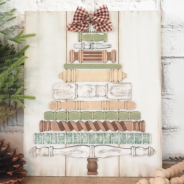 Bring a touch of nostalgia to your holiday décor with the Spindle Christmas Tree DIY Kit from Janet's Craft Corner. This rustic piece features a charming arrangement in shades of beige, green, and brown, crowned with a red plaid bow and complemented by a light wood background. Pine branches and a pinecone nearby add to its festive allure.